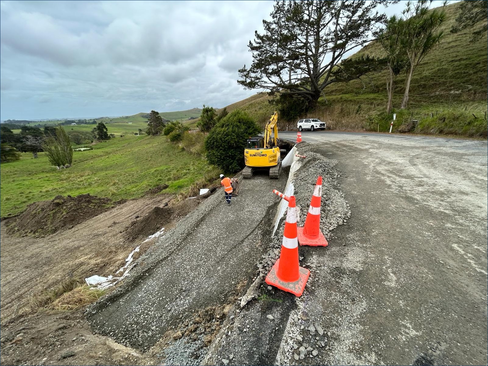 Unsealed road with yellow digger, cones and worker